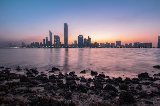 Stunning Abu Dhabi cityscape at sunrise with calm ocean foreground and vibrant sky.