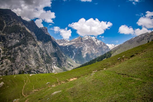 Breathtaking view of snow-capped mountains, green meadows, and a clear blue sky, perfect for nature lovers.