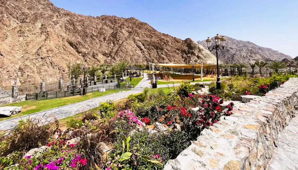 Shees Park in Sharjah: Waterfall, Timings, Things to Do and Nearby Hotels 3 Flower beds and stone walkway at Shees Park with the Hajar Mountains behind